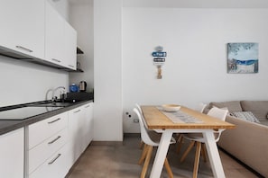 A modern kitchen with white cabinets, a black countertop, and a dining area with a wooden table and white chairs. - Comfortable Apartment Steps from the Sea - Marina di Carrara (Marina di Carrara)