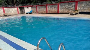 En swimmingpool med blå kant, metalgelændere og en stenvæg med røde detaljer i baggrunden.