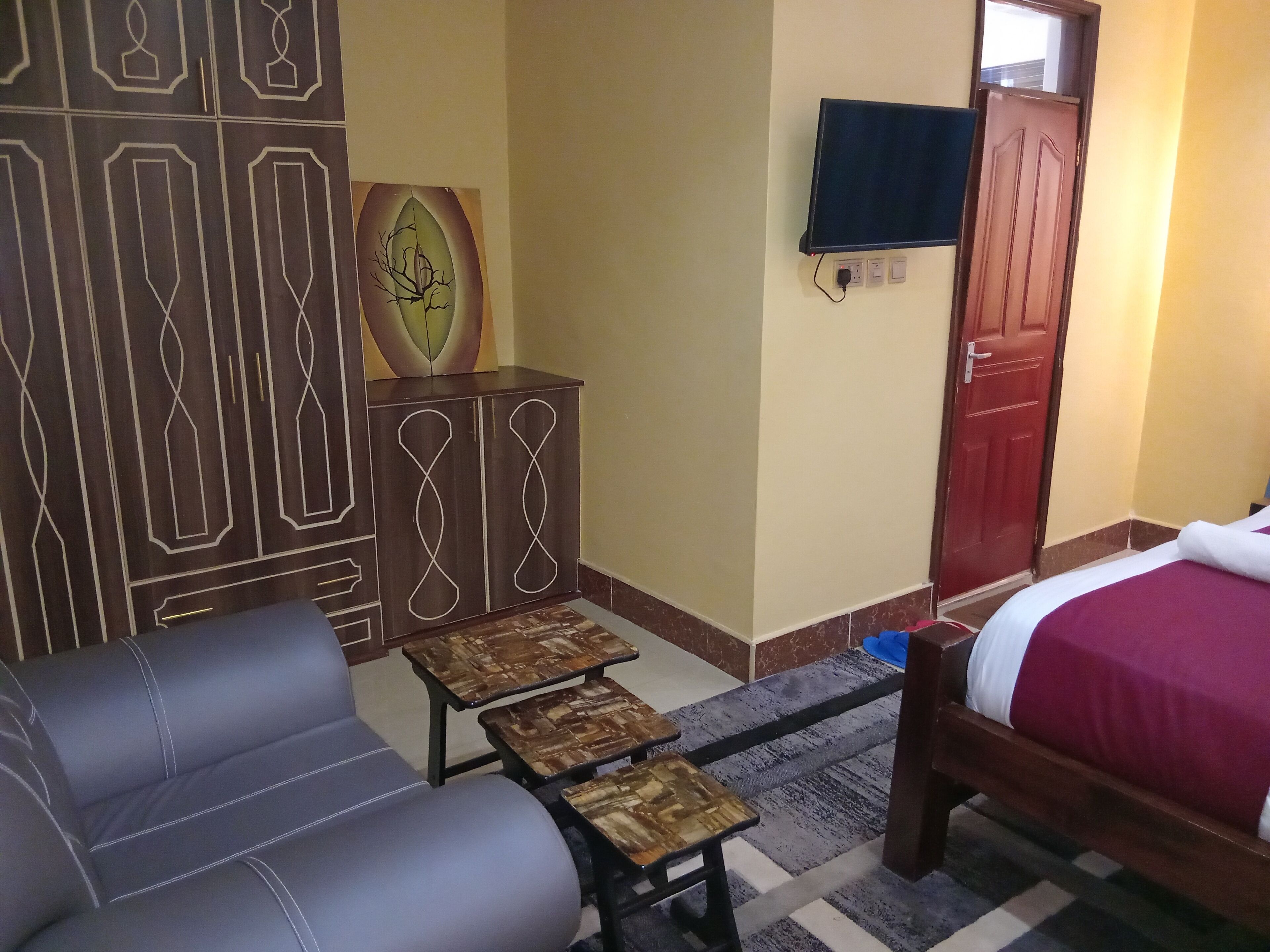 A room with a bed, a sofa, a small wooden table, a cabinet, and a television on the wall.