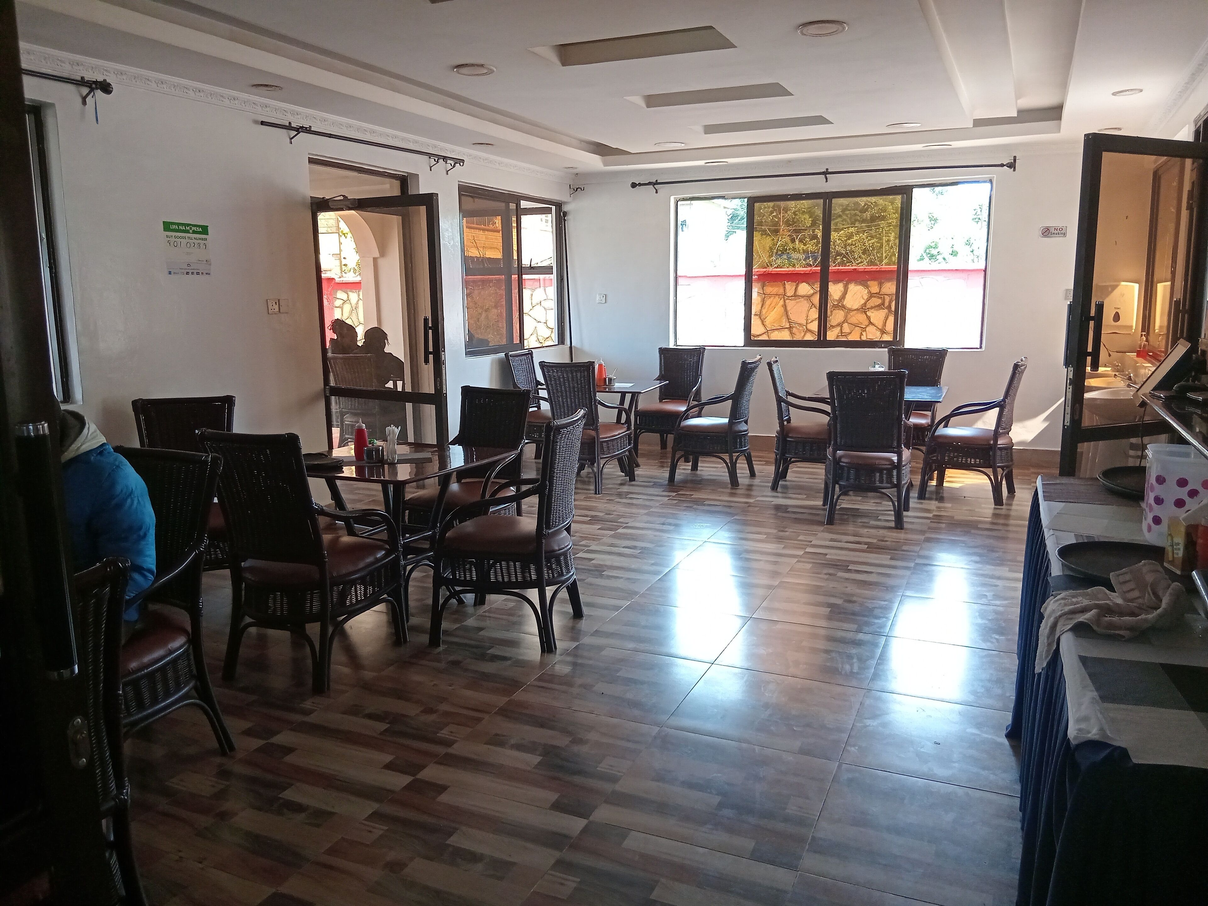 A spacious room with wooden flooring, wicker furniture, and large windows allowing natural light.