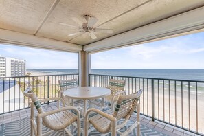 A balcony with a table and chairs, overlooking a beach and ocean. - Sandcastle 401 (New Smyrna Beach)