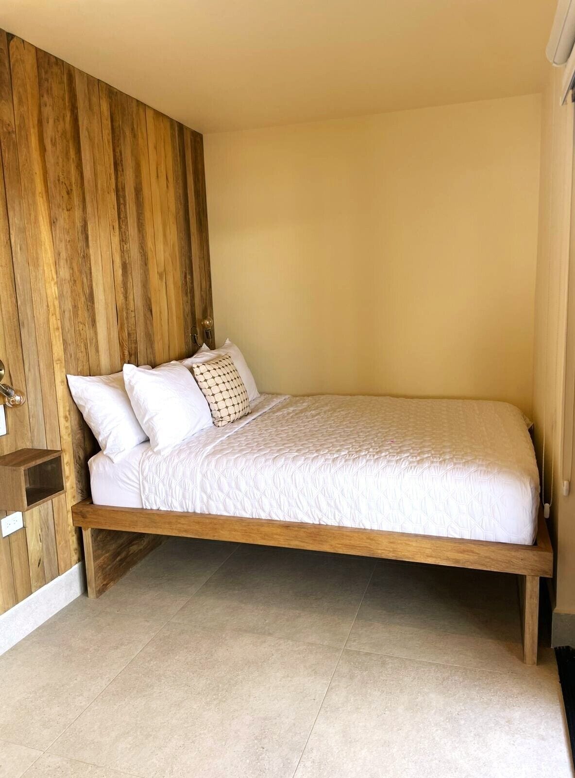 A single bed with a wooden headboard, white bedding, and a small bedside table with a lamp.