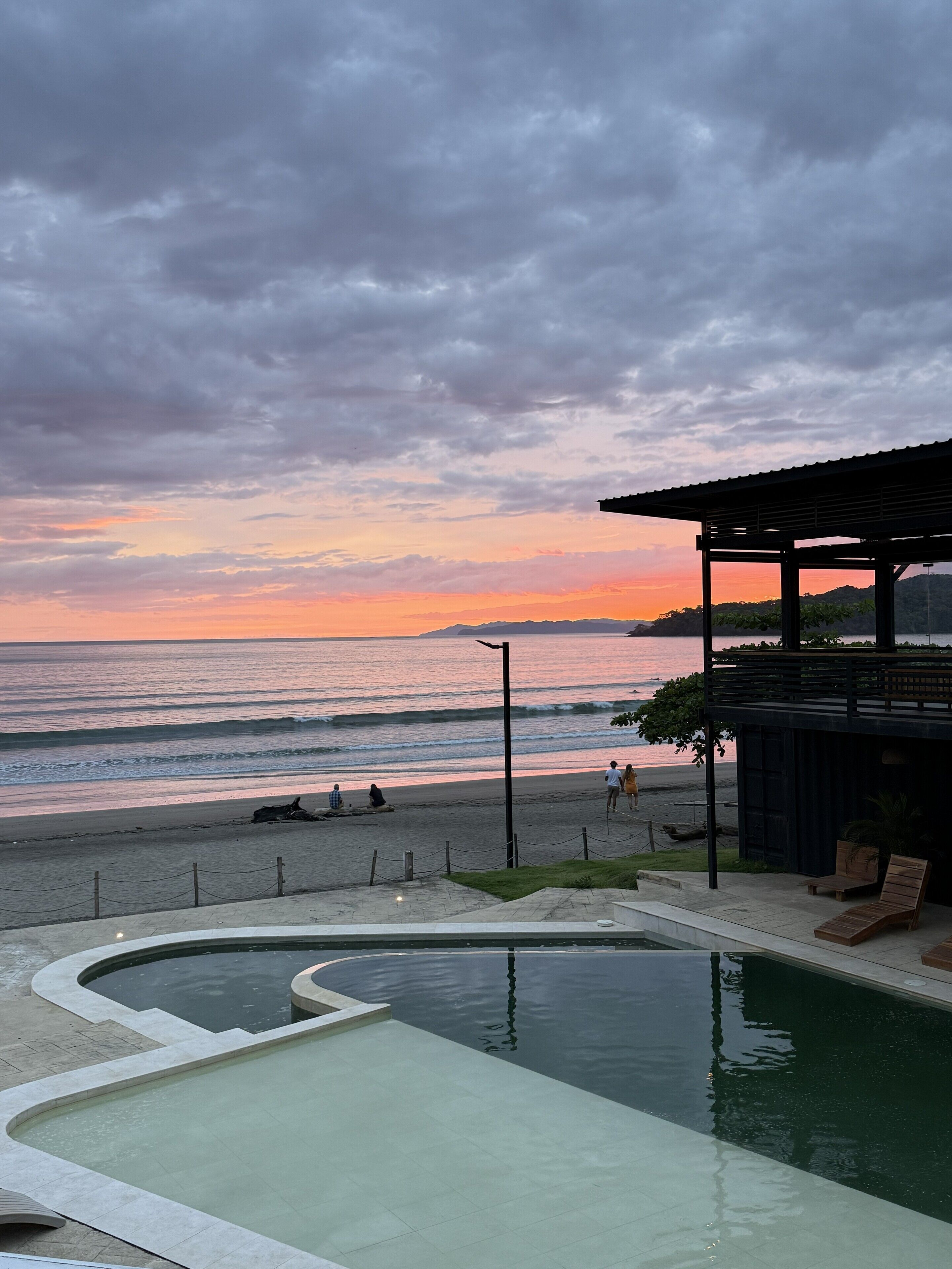 Une piscine avec vue sur la plage et l’océan au coucher du soleil.