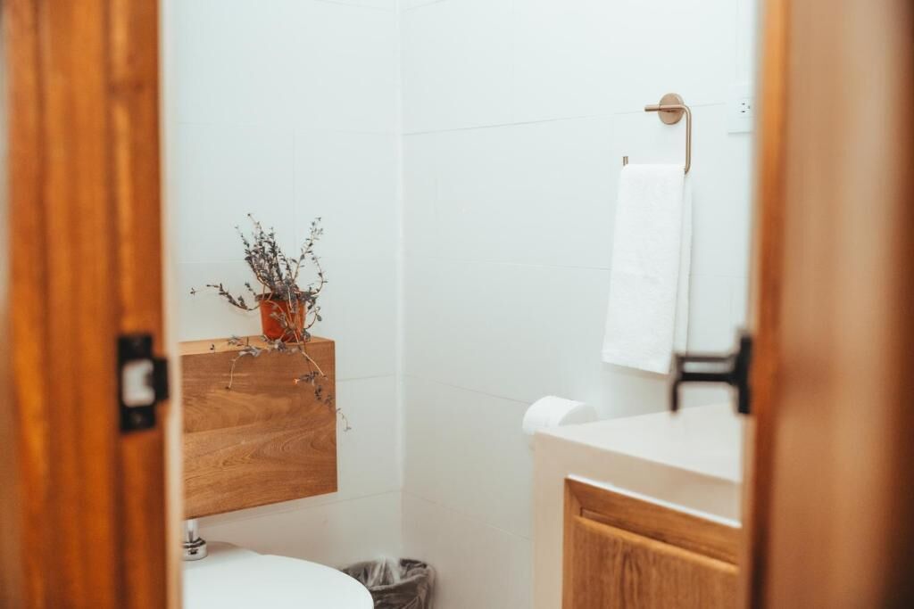 Une petite salle de bain propre, avec un meuble-lavabo en bois, des toilettes blanches et une plante en pot accrochée au mur.
