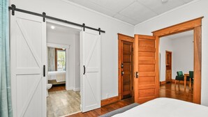 Ein Schlafzimmer mit einem Bett, einer Holztür und einer Schiebetür im Stil einer Scheune, die ins Bad führt.