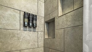 Ein modernes Badezimmer mit Duschbereich, einer Holzbank und drei Flaschen Shampoo und Conditioner an der Wand.