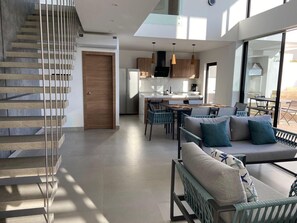 Un interior moderno con una escalera, un comedor y un espacio de sala con un sofá y sillones.