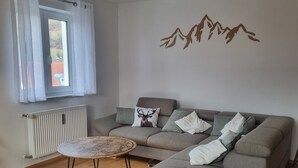 Een moderne woonkamer met een hoekbank, een ronde salontafel en een raam met gordijnen.