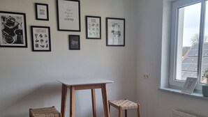 Een kamer met een witte tafel, twee houten krukken en een raam met uitzicht op zonnepanelen.