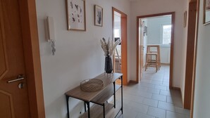 Een hal met een houten bankje, ingelijste foto's aan de muur en een betegelde vloer.