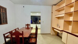 Un comedor con una mesa y sillas de madera, piso de baldosas y una cocina al fondo.