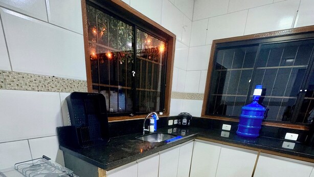 Una cocina con gabinetes blancos, estufa a gas, lavamanos y ventana con vista a árboles.