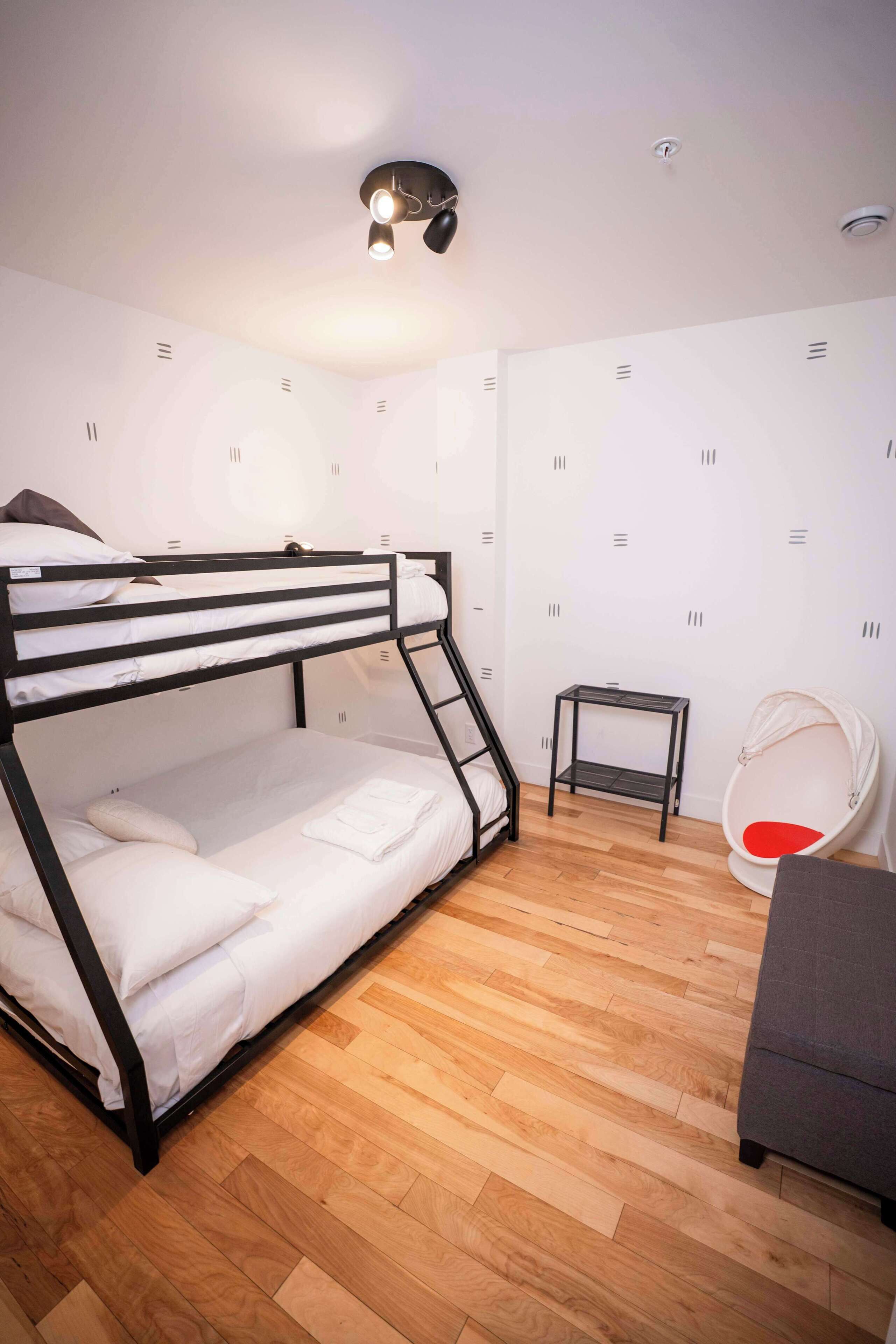 A bunk bed with a small table and a hanging chair in a room with wooden flooring and white walls.