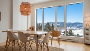 Ruokailutila, jossa on suuri pöytä, tuoleja ja näkymä lumiseen maisemaan suurista ikkunoista.