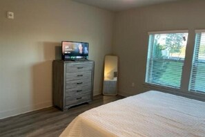 Quarto com cama, cômoda, televisão e janela com persianas.