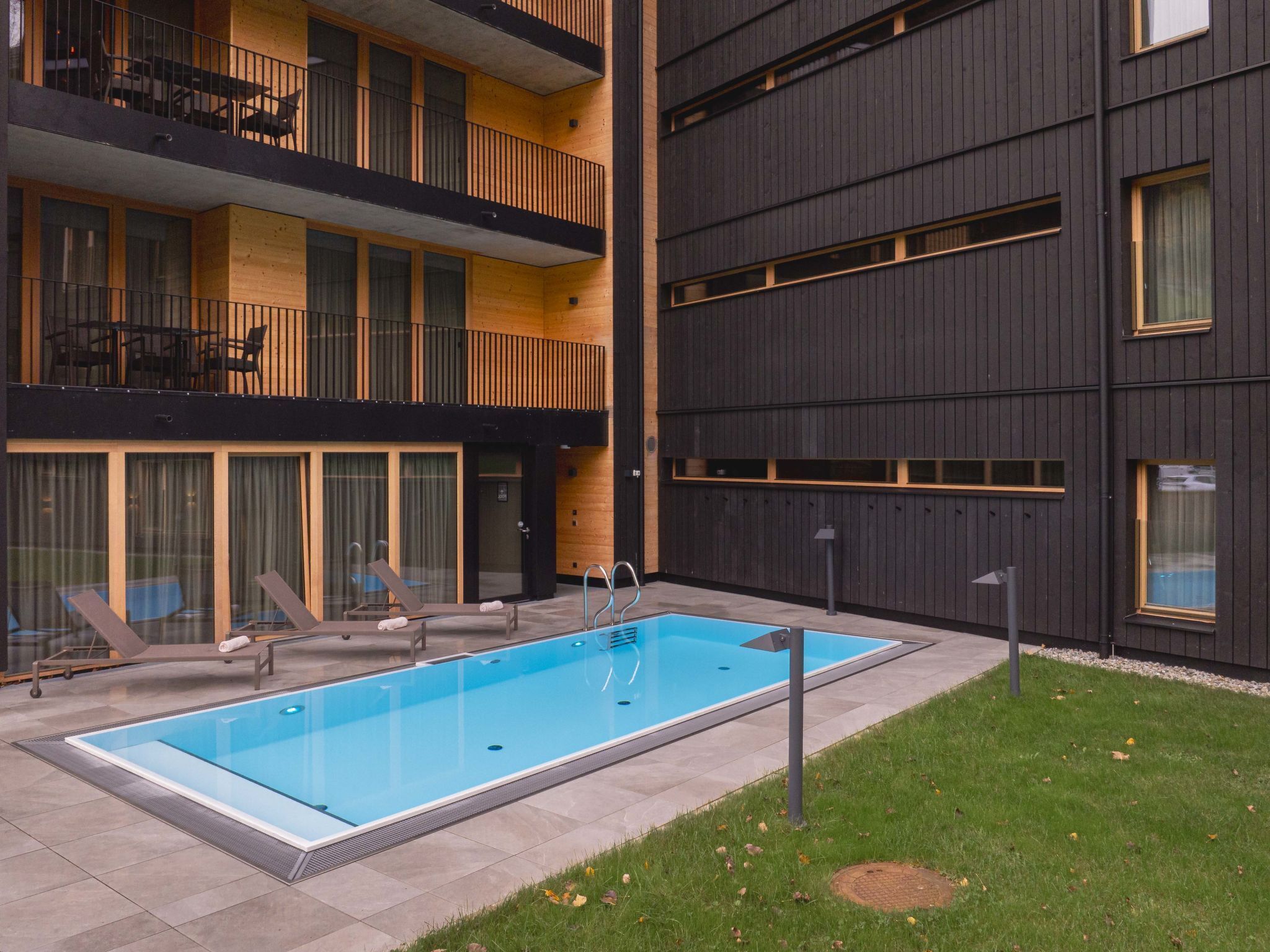 Un edificio moderno con piscina, asientos exteriores y un césped bien cuidado.