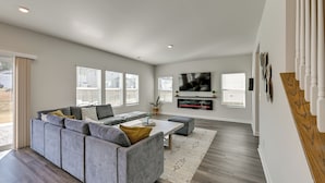Un salon spacieux avec un canapé d’angle gris, une table basse et un téléviseur à écran plat fixé au mur.