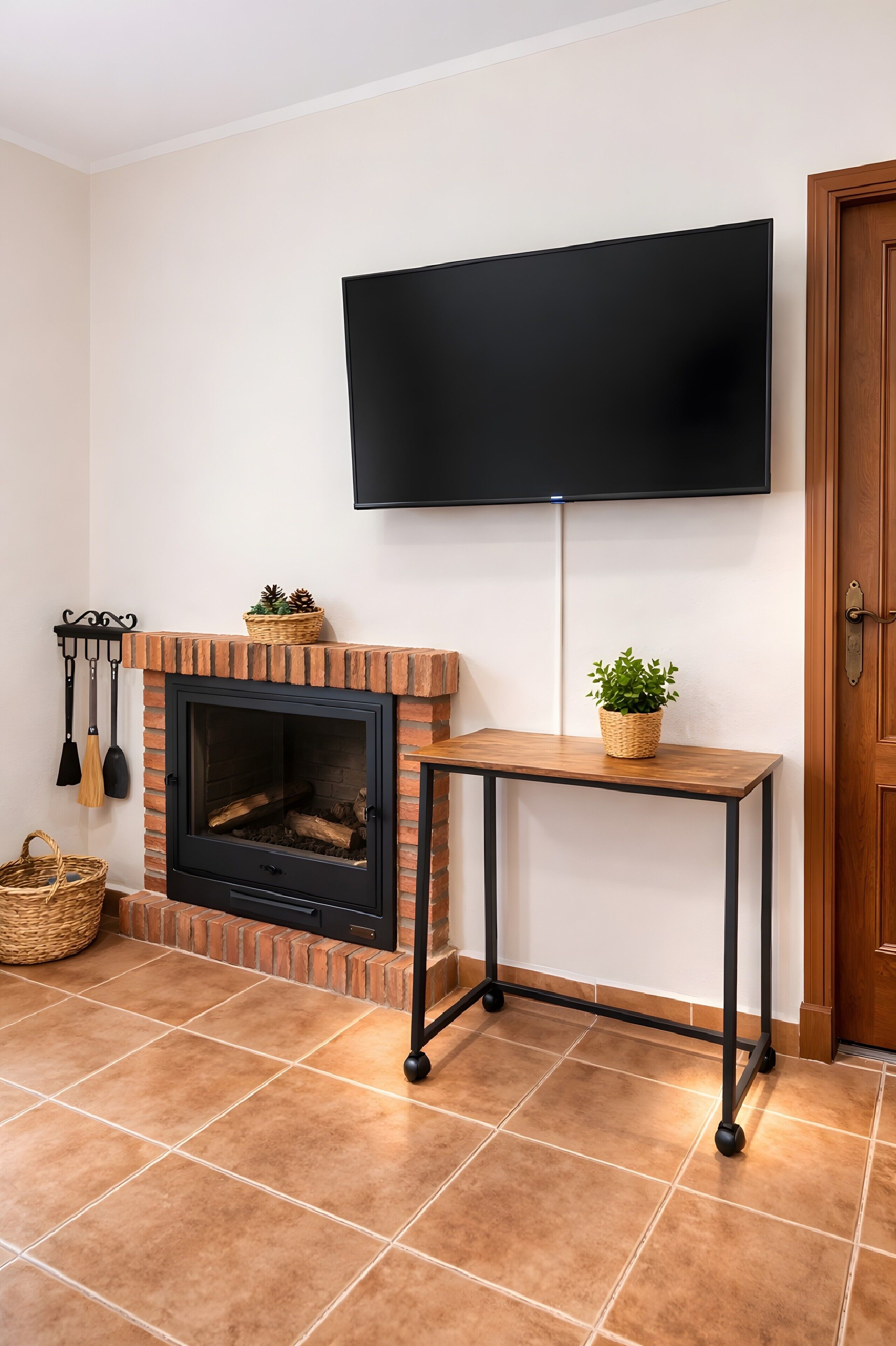 Una chimenea con un televisor montado encima, una mesa de madera al lado de la chimenea y una puerta a la derecha.