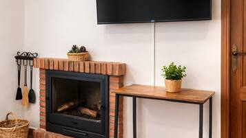 Una chimenea con un televisor montado encima, una mesa de madera al lado de la chimenea y una puerta a la derecha.