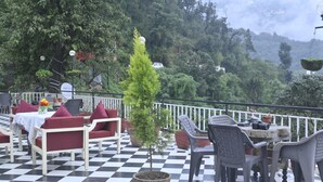 A terrace with checkered flooring, outdoor seating, potted plants, and a view of a mountainous landscape. - The Perfect Hideout By Himalayan Grove (Dehradun)