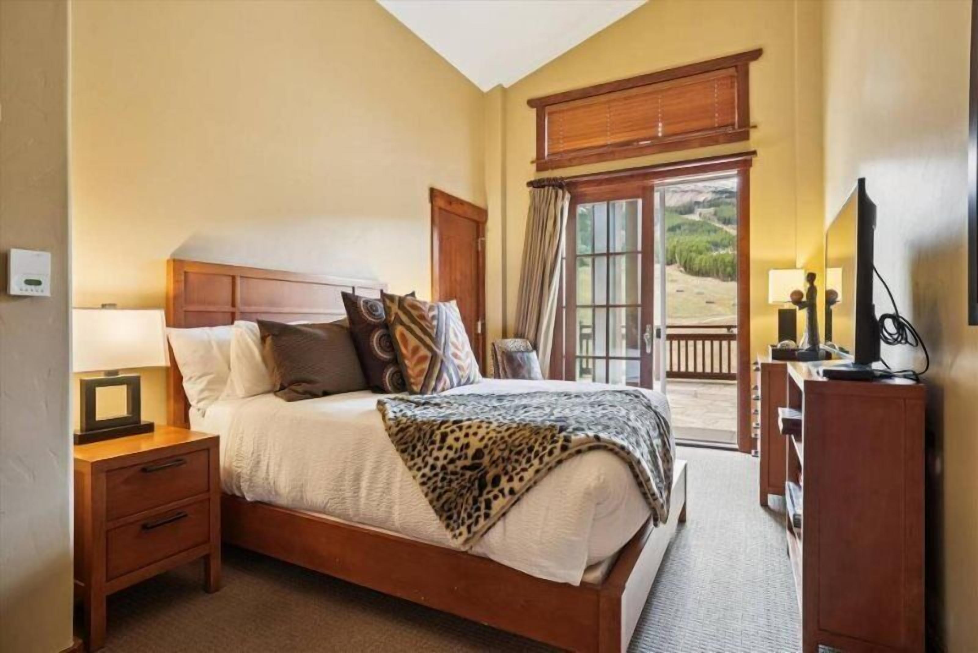 Un dormitorio con una cama de madera, una mesita de noche, un escritorio y vistas al exterior.
