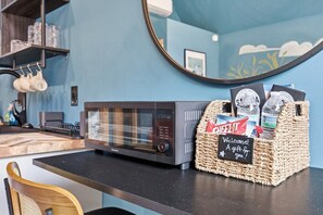 A kitchen area with a microwave, a wicker basket labeled 'Welcome Gift for you!', and a mirror on the wall.