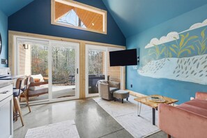 A room with a large sliding glass door leading to a deck, a mounted flat-screen TV, and a ceiling with a skylight.
