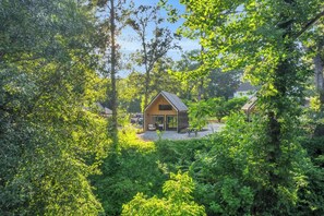 Ein kleines, eingeschossiges Haus, umgeben von dichtem Grün, mit blauem Himmel.