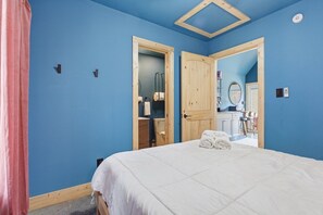 A bedroom with a large bed, wooden doors, and a bathroom visible through an open door. - The Blue Heron - Riverfront Retreat w/ Hot Tub (Easley)