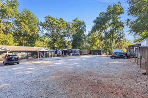 A gravel parking area with multiple vehicles, a building with a garage, and a row of trees in the background.
