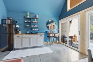 A compact kitchen with a refrigerator, microwave, and cabinets, a dining area with chairs, and a large window providing natural light. - The Blue Heron - Riverfront Retreat w/ Hot Tub (Easley)