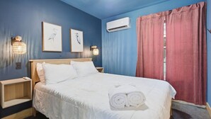 A hotel room with a bed, bedside tables, wall-mounted air conditioning, and curtains.