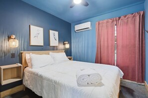 A hotel room with a bed, bedside tables, wall-mounted air conditioning, and curtains.