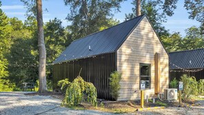 A small wooden building with a sloped roof, surrounded by trees and a gravel area.