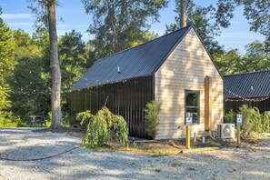 A small wooden building with a sloped roof, surrounded by trees and a gravel area.