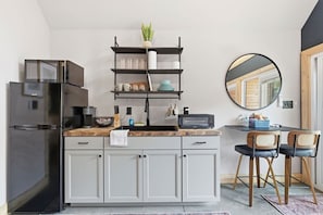 A compact kitchen with a black refrigerator, a built-in microwave, a wooden countertop, and a three-tiered shelf unit. - The Kingfisher - Private Hot Tub, Riverfront Cabin (Easley)