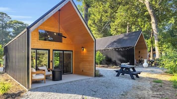 A modern cabin with a sloped roof, large windows, and a patio area with seating.