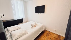 Ein Schlafzimmer mit Bett, Schreibtisch, Stuhl, Fernseher und einem Fenster mit Vorhängen.