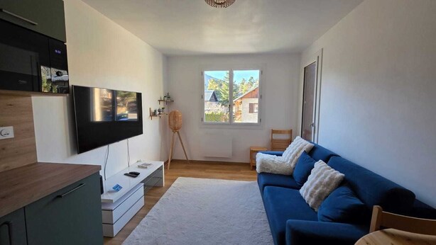 A modern living room with a flat-screen TV, a blue sofa, a white rug, and a wooden floor. - Charming apartment overlooking the valley (Briançon)