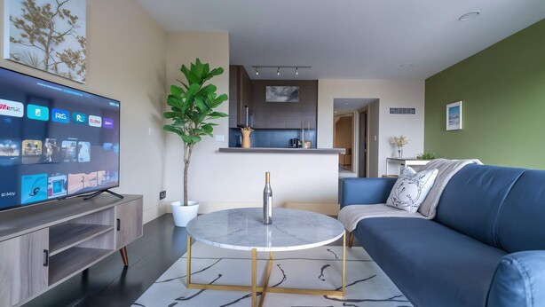 A modern living room with a flat-screen TV, a round coffee table, a blue sofa, and a potted plant. - Boulevard Stays Relaxed 1BR King Suite Near Downtown, Pool & Gym Access (Austin)