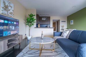 A modern living room with a flat-screen TV, a round coffee table, a blue sofa, and a potted plant. - Boulevard Stays Relaxed 1BR King Suite Near Downtown, Pool & Gym Access (Austin)