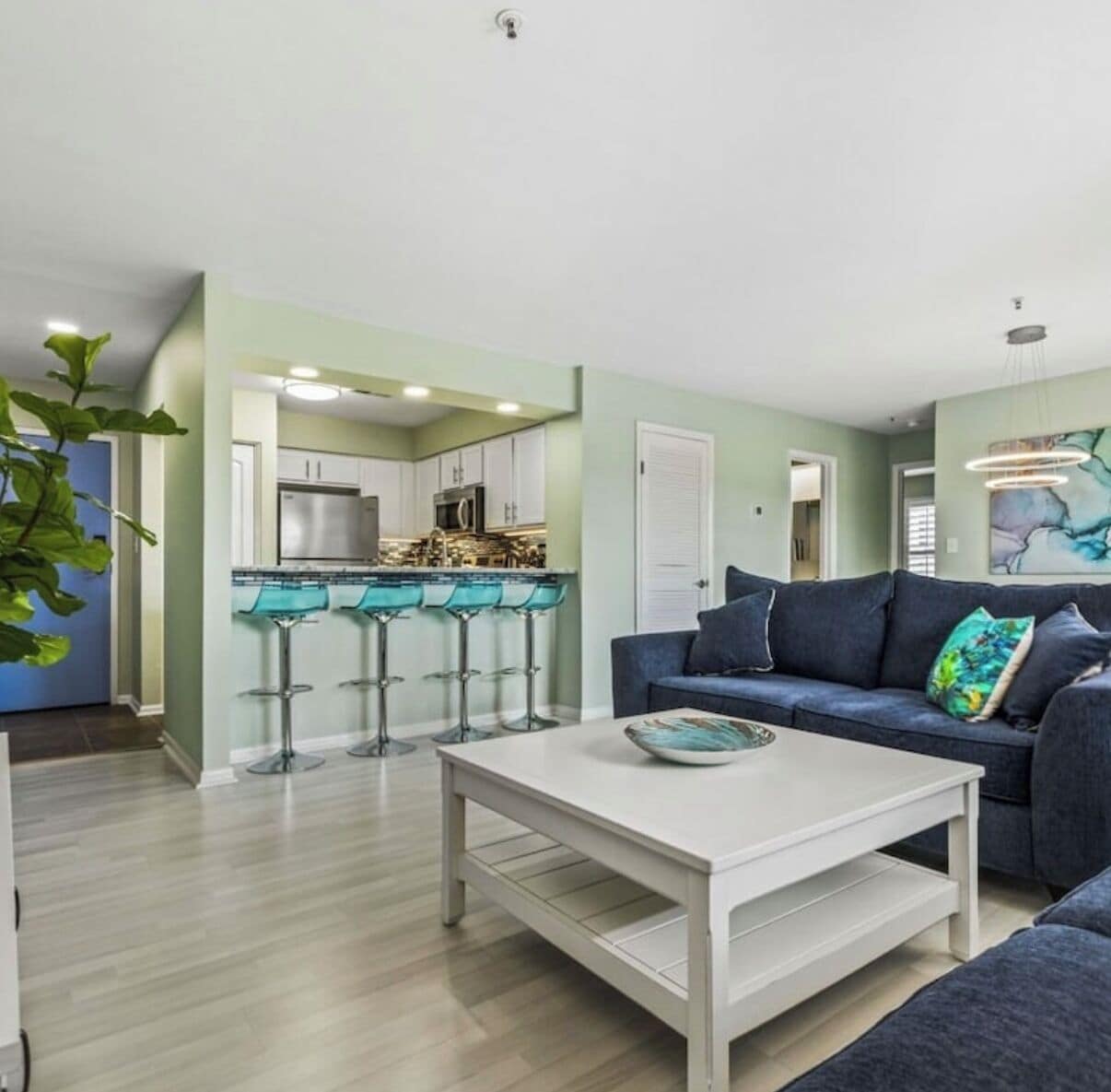 Een moderne woonkamer met een donkerblauwe bank, een witte salontafel en een keukenhoek met een barset.