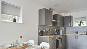 A modern kitchen with grey cabinets, a wooden countertop, and a dining area with white chairs and a table set for four. - Student Only The Quarry (Falmouth)