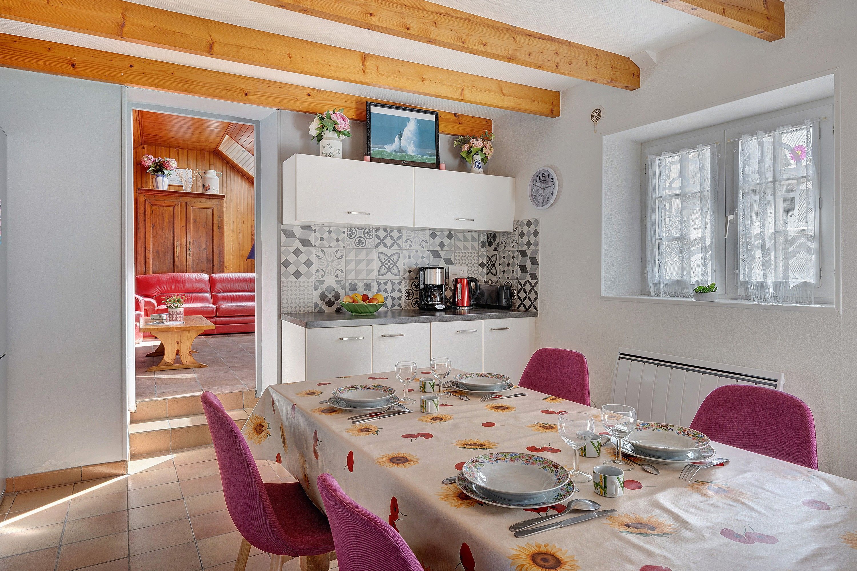 A dining area with a table set for four, a kitchen in the background, and a red sofa in the living area.