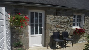 A stone building with a white door, two windows, and a small porch with two chairs. - Ground-Floor Stone Cottage Between Countryside and Sea (Landunvez)