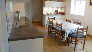 A modern kitchen with a dining area, featuring a sink, stove, and a table with chairs. - Ground-Floor Stone Cottage Between Countryside and Sea (Landunvez)