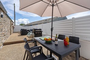Eine Terrasse im Freien mit Tisch, Stühlen, einem Grill und einem weißen Zaun.