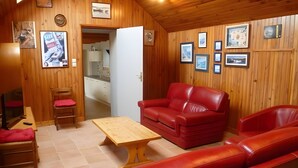 A wooden-paneled room with a red leather sofa, a wooden coffee table, and a red cushioned chair. - Ground-Floor Stone Cottage Between Countryside and Sea (Landunvez)