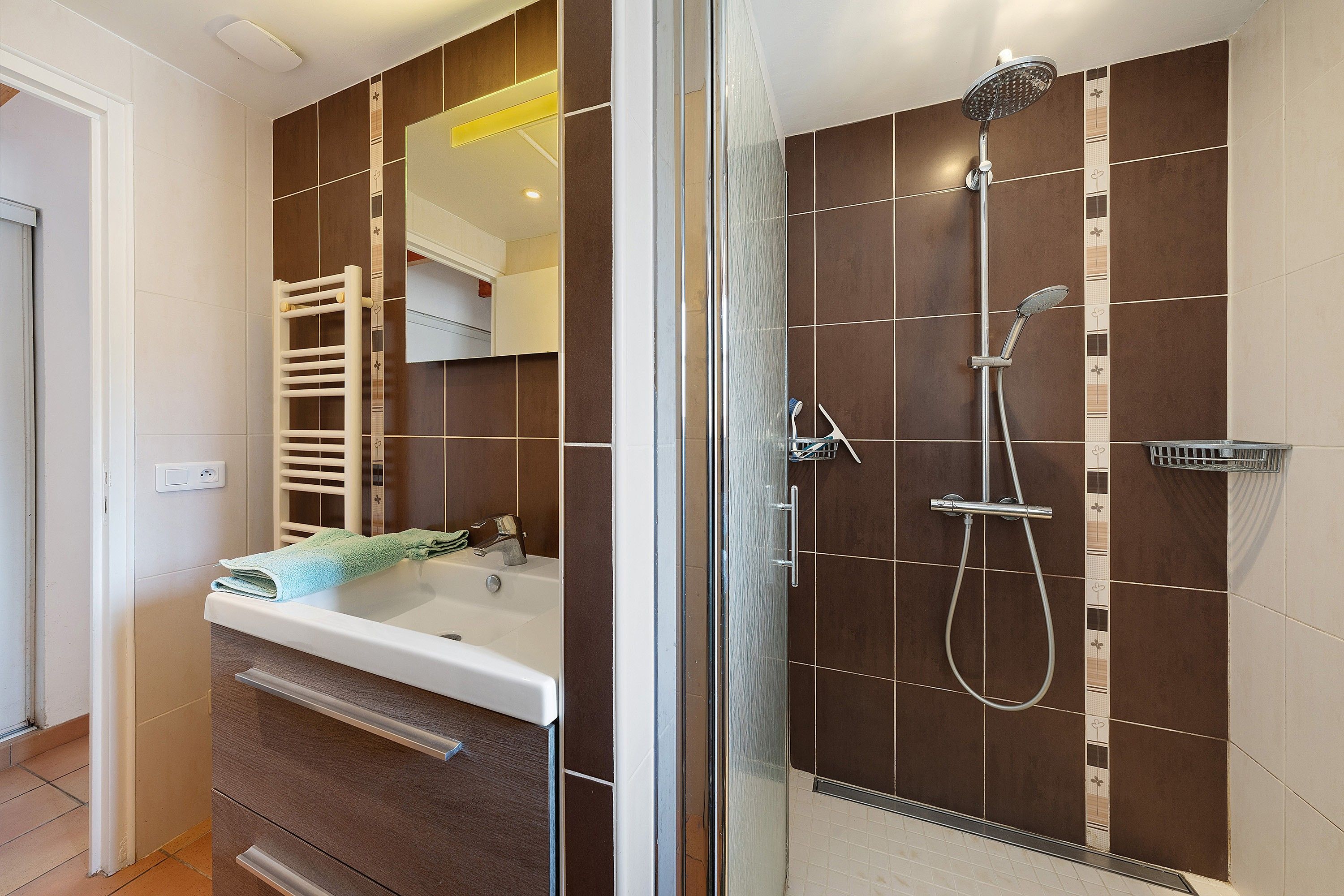 Een moderne badkamer met een douchecabine van glas, een witte wastafel en een handdoekrek.