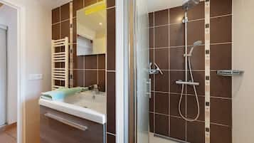 Een moderne badkamer met een douchecabine van glas, een witte wastafel en een handdoekrek.